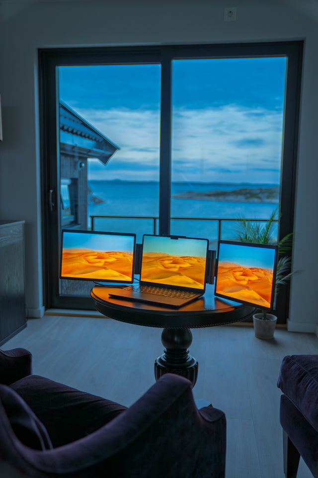 Tre skjermer på et stuebord med utsikt gjennom vinduet