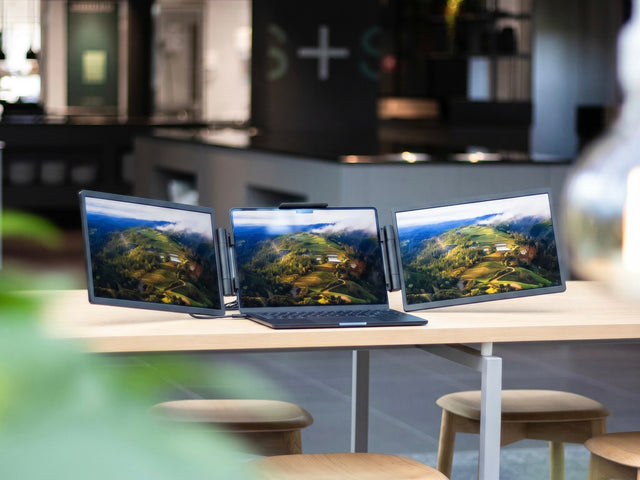 Laptop with two extra screens on a bright desk in a coworking space